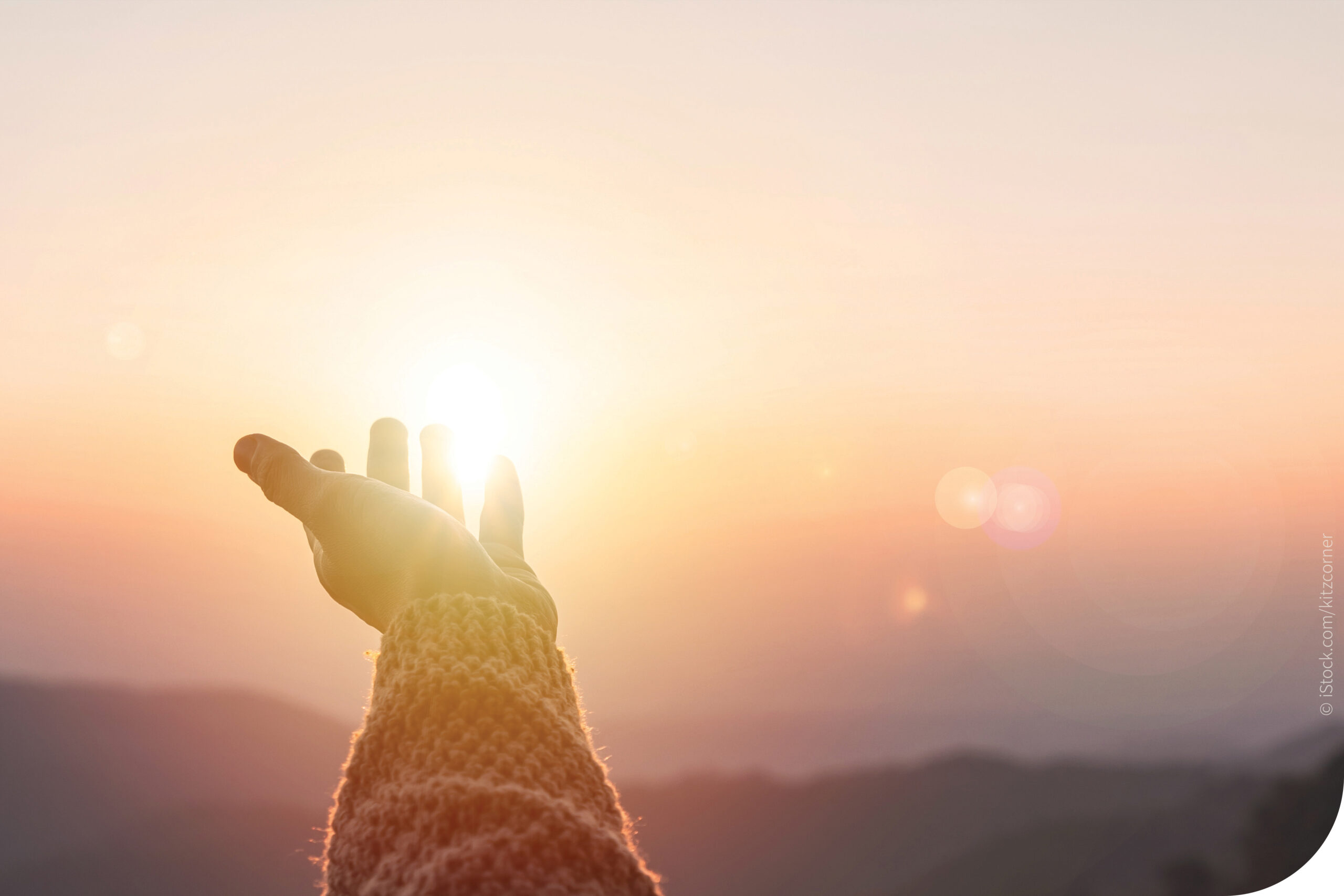 Eine Hand wird Richtung Sonnenaufgang gestreckt.