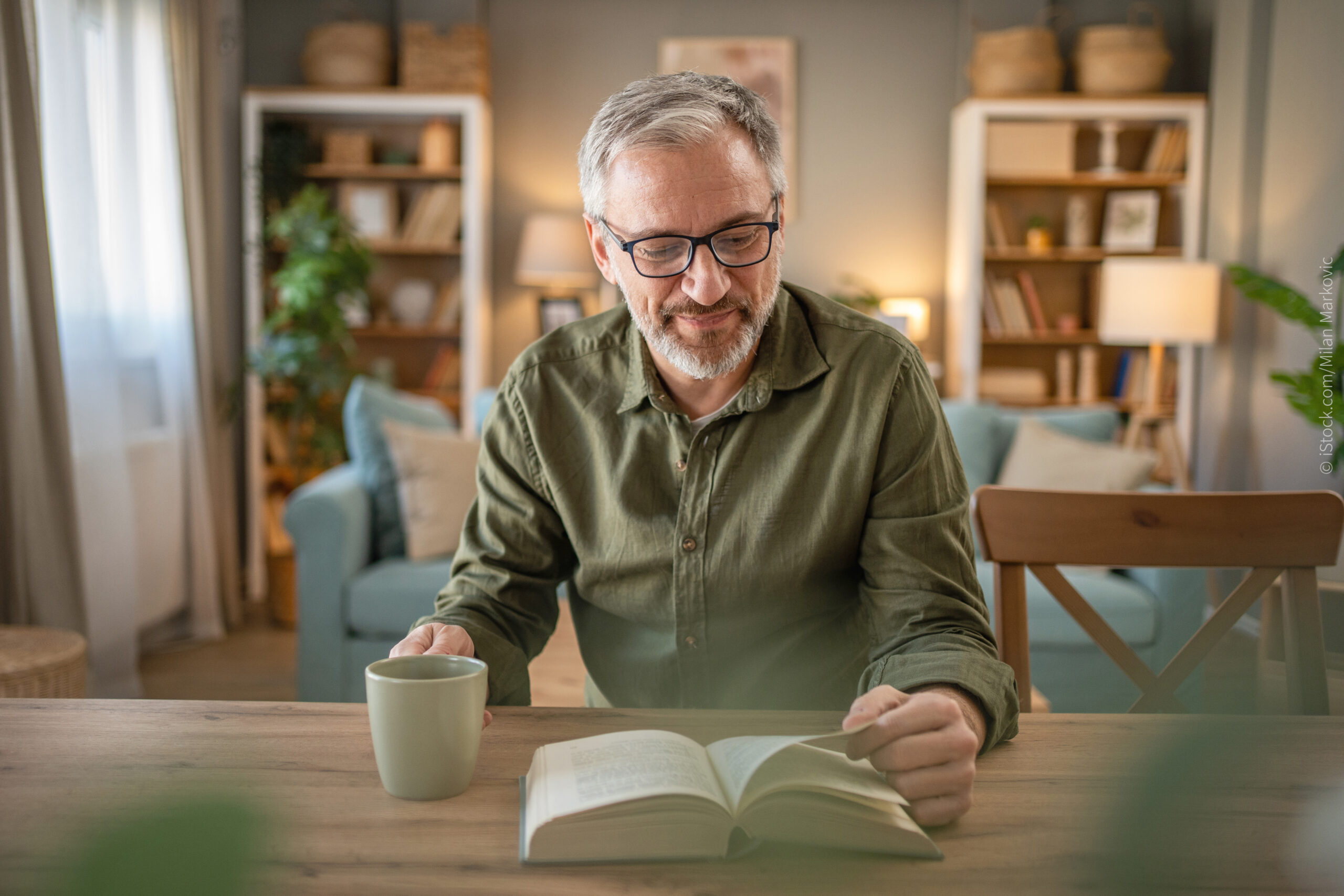 Ein alter Mann liest mit einer Tasse Tee ein Buch zum Thema: Liebt mich Gott